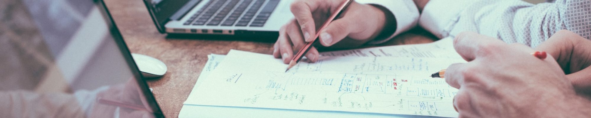 person holding pencil near laptop computer